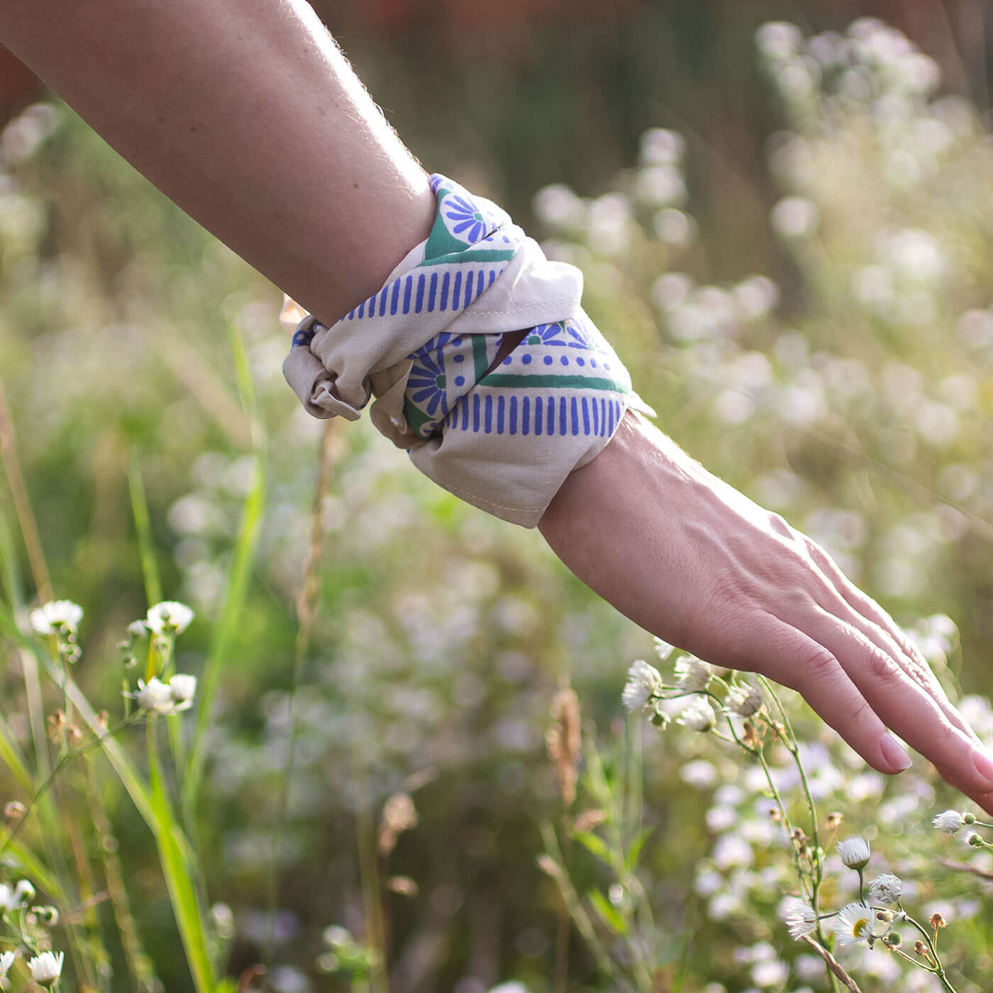 Hand wearing a colorful bandana in a natural setting with greenery and flowers.