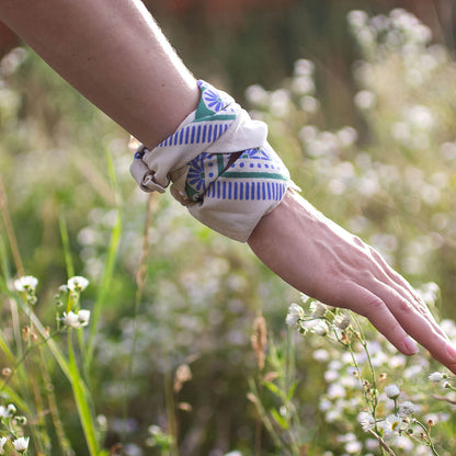 Hand wearing a colorful bandana in a natural setting with greenery and flowers.
