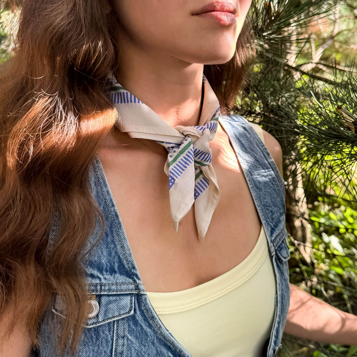 Woman wearing a patterned bandana outdoors with greenery in the background