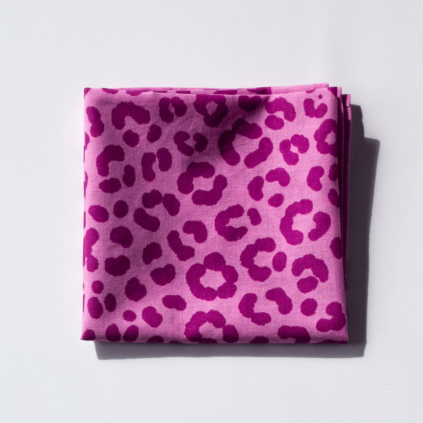 Folded pink bandana with leopard print pattern on a light gray background