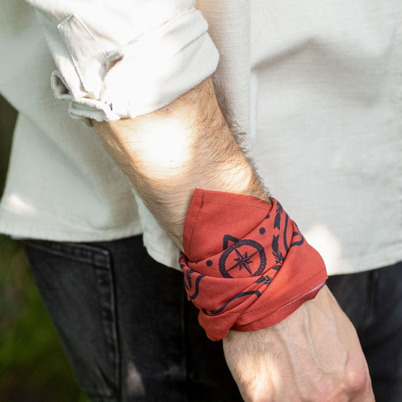 Man wearing a red bandana wristband with black design on a blurred outdoor background