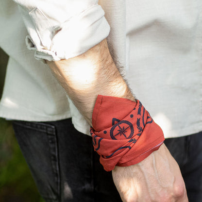 Man wearing a red bandana wristband with black design on a blurred outdoor background