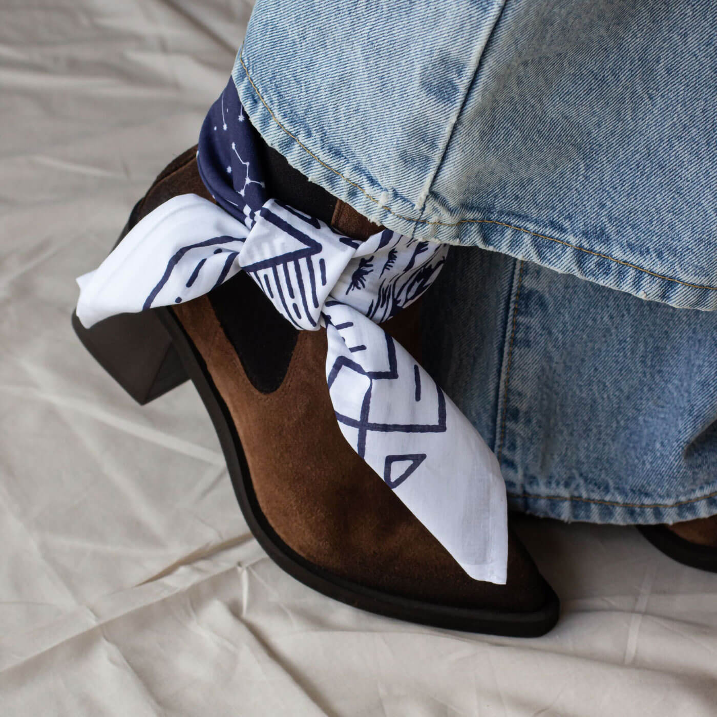Brown suede pointed toe chelsea boot with a white bandana and blue jeans on a beige surface