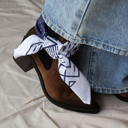 Brown suede pointed toe chelsea boot with a white bandana and blue jeans on a beige surface